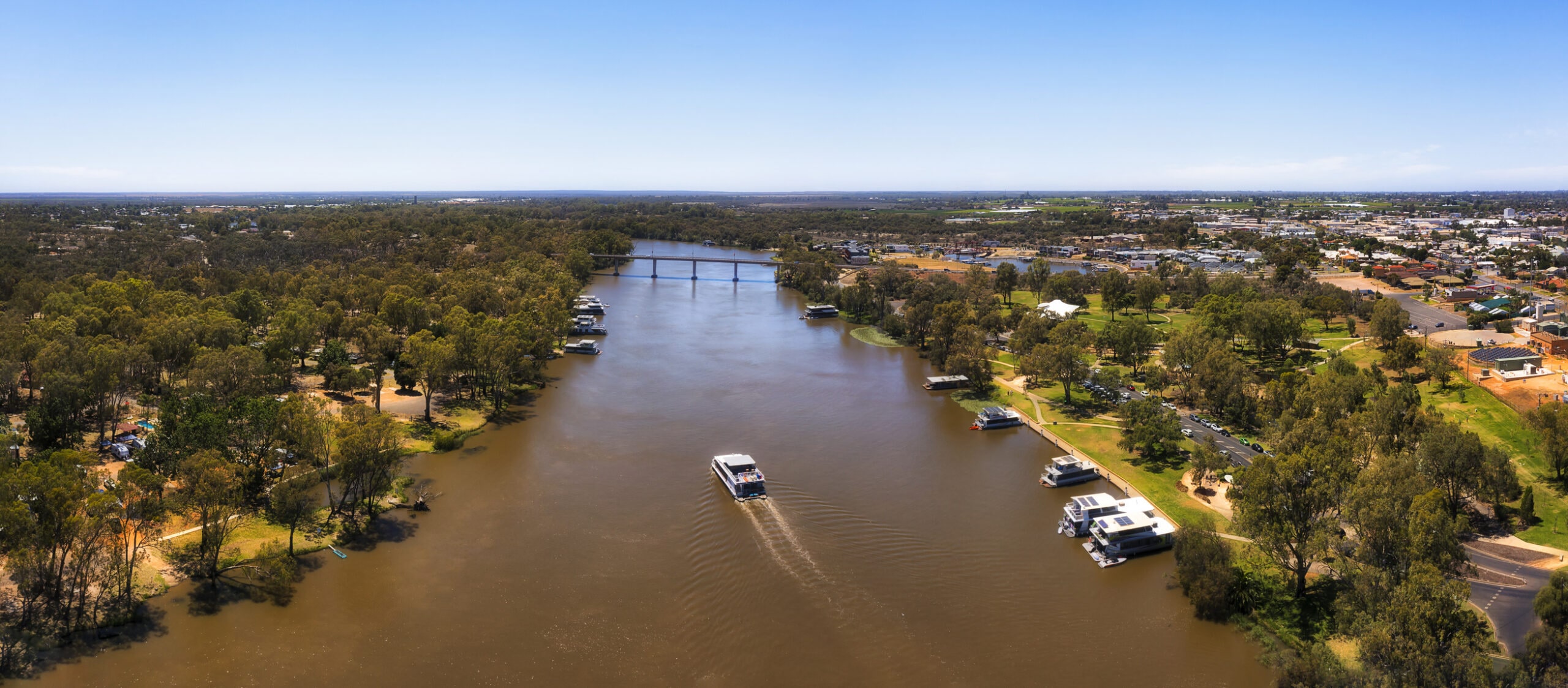 Wide Murray river at Mildura city of Australian Riverina in aerial panorama with cruise boat.
